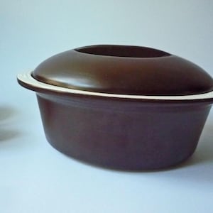 Peut inclure: Un plat à casserole en céramique marron avec un couvercle. Le plat a un bord blanc et un extérieur marron foncé. Le couvercle a une forme arrondie avec un centre en retrait. Conçu pour la cuisine et le service.