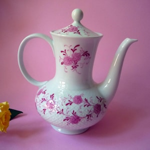 Peut inclure: Une théière en porcelaine blanche ornée d'un motif floral magenta délicat et d'un relief en forme de losanges sur le corps. La théière comprend un couvercle assorti avec un petit bouton, un bec verseur courbé et une anse arrondie.
