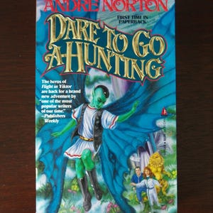 May include: A paperback book by Andre Norton, titled "DARE TO GO A-HUNTING". The cover shows a green-skinned figure with blue wings, and other figures. The background is blue with gold lettering. The book is a "First Time in Paperback".