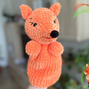 May include: A handmade orange crochet fox puppet with a black nose and eyes. The puppet has a smiling expression and is made of soft, textured yarn. The image includes the text "crochet pattern PDF".