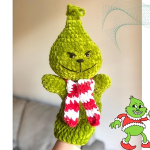 Puede incluir: Una marioneta verde hecha a mano con el tema del Grinch y una bufanda a rayas rojas y blancas. La marioneta tiene una cara sonriente y está hecha de un material suave y texturizado. La imagen también incluye una ilustración de dibujos animados del Grinch y el texto "English pattern PDF".