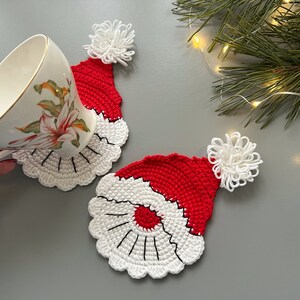 K&ouml;nnte beinhalten: Zwei geh&auml;kelte Weihnachtsmann-Hut-Untersetzer in Rot und Wei&szlig;. Die Untersetzer sind aus Garn gefertigt und haben einen wei&szlig;en Bommel oben drauf.