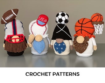 May include: Four crocheted gnomes, each representing a different sport. The first gnome wears a football helmet and has a brown beard. The second gnome wears a baseball cap with "USA" embroidered on it and has a blue beard. The third gnome wears a black hat with a white "X" on it and has a blue beard. The fourth gnome wears a basketball and has a brown beard. The gnomes are all standing on a gray surface. CROCHET PATTERNS is written in black text below the gnomes.