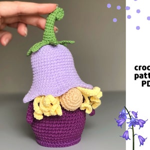 Könnte beinhalten: Häkelanleitung PDF für einen lila und grünen Gnome mit gelbem Bart. Der Gnome trägt einen lila Hut mit einem grünen Stiel.