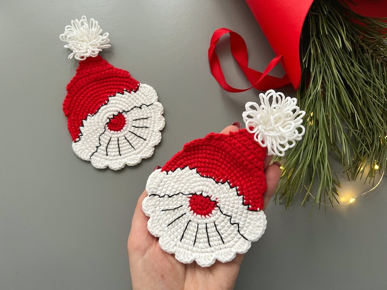 K&ouml;nnte beinhalten: Zwei geh&auml;kelte rote und wei&szlig;e Weihnachtsm&uuml;tzen mit wei&szlig;en Bommeln. Die M&uuml;tzen sind aus wei&szlig;em und rotem Garn gefertigt und haben einen schwarzen Umriss.