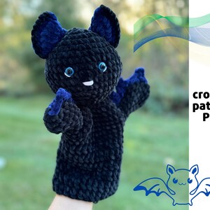 May include: Crochet pattern PDF for a black bat puppet with blue ears and eyes. The puppet is on a hand with a green background.