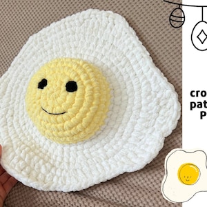 K&ouml;nnte beinhalten: Ein wei&szlig;es geh&auml;keltes Ei mit einem gelben Eigelb, das wie ein l&auml;chelndes Gesicht geformt ist. Das Ei liegt auf einer braunen Oberfl&auml;che. Der Text "crochet pattern PDF" befindet sich in der oberen rechten Ecke des Bildes.