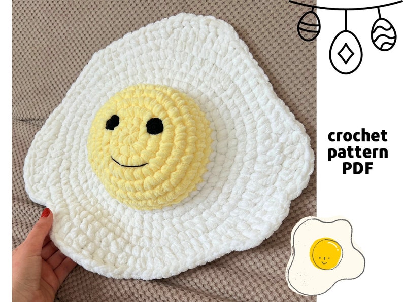K&ouml;nnte beinhalten: Ein wei&szlig;es geh&auml;keltes Ei mit einem gelben Eigelb, das wie ein l&auml;chelndes Gesicht geformt ist. Das Ei liegt auf einer braunen Oberfl&auml;che. Der Text "crochet pattern PDF" befindet sich in der oberen rechten Ecke des Bildes.