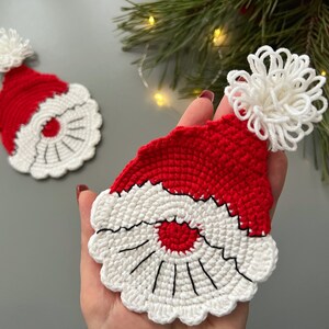 K&ouml;nnte beinhalten: Zwei geh&auml;kelte Weihnachtsm&uuml;tzen mit wei&szlig;en Bommeln. Die M&uuml;tzen sind rot und wei&szlig; mit einem schwarzen Umriss um das Gesicht.
