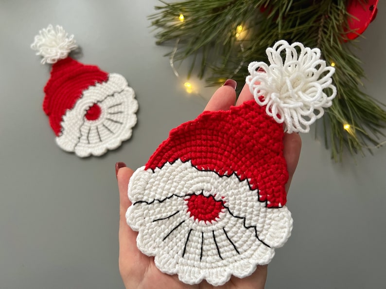 K&ouml;nnte beinhalten: Zwei geh&auml;kelte Weihnachtsm&uuml;tzen mit wei&szlig;en Bommeln. Die M&uuml;tzen sind rot und wei&szlig; mit einem schwarzen Umriss um das Gesicht.