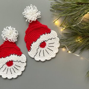 K&ouml;nnte beinhalten: Zwei geh&auml;kelte Weihnachtsm&uuml;tzen mit wei&szlig;en Bommeln. Die M&uuml;tzen sind rot und wei&szlig; mit einem wei&szlig;en H&auml;kelrand um den Rand.