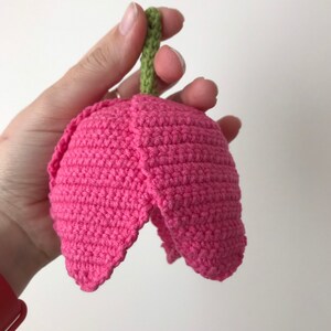 May include: A pink crocheted tulip flower with a green stem. The flower is crocheted in a single crochet stitch and has a rounded shape.