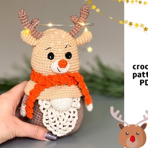 May include: Crochet pattern PDF for a cute reindeer amigurumi toy. The reindeer is brown with a white face, orange scarf, and white crocheted antlers.