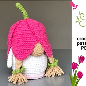 May include: Crochet pattern PDF for a pink and white gnome with a flower hat and braided hair.