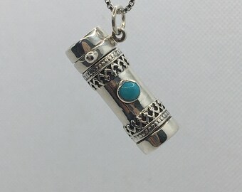 May include: A silver pendant necklace with a cylindrical charm featuring intricate designs and a turquoise stone.