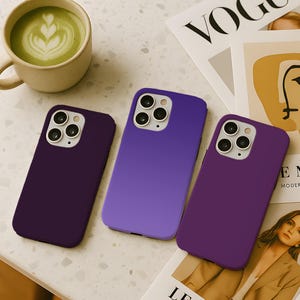 May include: Three purple phone cases in varying shades of plum and violet are displayed on a speckled surface. A cup of matcha latte and a magazine are also present. The phone cases have multiple camera cutouts.