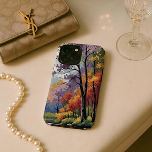 May include: A smartphone case featuring a colorful autumn forest scene with trees in shades of orange, yellow, and purple. The case is black around the camera lenses. A beige purse and a pearl necklace are also in the image.