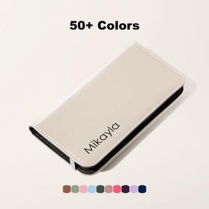 Könnte beinhalten: Ein cremefarbenes Etui mit dem Aufdruck "Mikayla". Das Etui hat einen schwarzen Rand und einen silbernen Verschluss. Der Text "50+ Colors" wird oben angezeigt, mit einer Farbpalette unten.