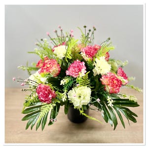 May include: A bouquet of pink and white carnations arranged in a black vase with green foliage.