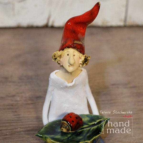 Sitting dwarf with a red hat holding ladybird, Pottery statuette, Clay figurine of leprechaun, Hand made gnom.