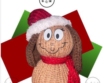 May include: A knitted dog snowman wearing a red and white Santa hat and a red scarf. The dog has brown ears and a smiling face. The image includes the text "Christmas dog Snowman Knitting Machine Recipe".