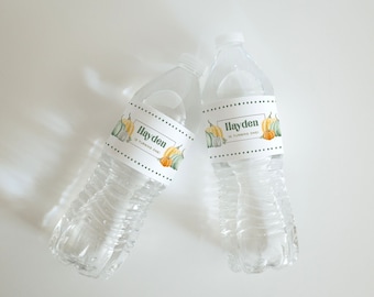 May include: Two clear plastic water bottles with white labels featuring a pumpkin theme. The labels say "Hayden is turning one!" and feature a green and orange pumpkin design.