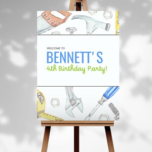 Könnte beinhalten: Ein weißes Schild auf einer Holzstaffelei mit dem Text "Welcome to Bennett's 4th Birthday Party!" in Blau und Grün. Das Schild ist mit Aquarellillustrationen von Werkzeugen verziert, darunter eine Säge, ein Hammer und ein Schraubenschlüssel.