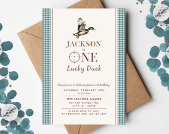 Puede incluir: Una invitación de fiesta de primer cumpleaños para un niño llamado Jackson. La invitación tiene un patrón de cuadros azules y blancos con un borde marrón. La invitación presenta un pato de dibujos animados con un objetivo detrás y el texto "Jackson tiene un año, un pato con suerte".