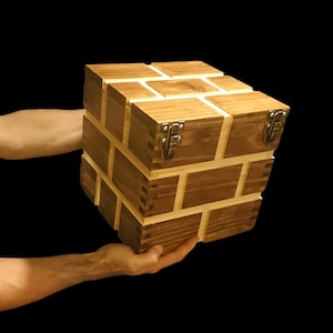 Puede incluir: Una caja de madera con un patrón de ladrillo y dos cierres metálicos. La caja está hecha de madera oscura con detalles en madera clara.