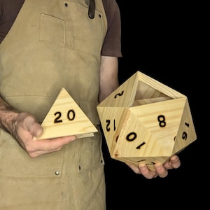 May include: A person holding two wooden dice. The larger die is a 12-sided die with the numbers 1, 2, 5, 6, 7, 8, 9, 10, 11, and 12 visible. The smaller die is a 20-sided die with the number 20 visible.
