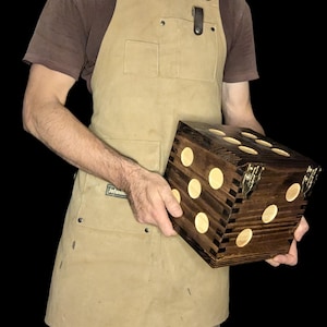 Puede incluir: Una gran caja de dados de madera con una mancha marrón oscura y puntos blancos. La caja está hecha de varias piezas de madera, creando un patrón único. La caja tiene bisagras de latón y un pestillo.