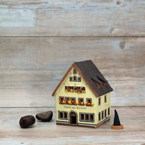 May include: A miniature ceramic house with a cream-colored facade, brown roof, and decorative flower boxes. The house features the text "Gasthof zum Breiterle" and is accompanied by chestnuts and a small green tree.