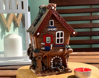 May include: A ceramic house figurine with a red roof, white trim, and a red door. The house is decorated with green vines and a chimney. The figurine is sitting on a wooden surface.