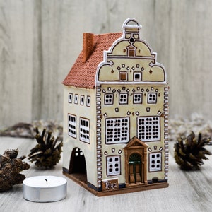 May include: A ceramic model of a building with a red roof and white trim. The building has multiple windows and a sign that reads "Riga".
