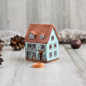 Może przedstawiać: Mały, ręcznie malowany ceramiczny domek z brązowym dachem i zielonymi ścianami. Domek ma okna i drzwi, a na froncie namalowane są słowa "Ella's".