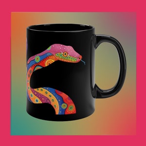 Könnte beinhalten: Eine schwarze Kaffeetasse mit einem bunten Schlangendesign. Die Schlange ist rosa, rot, orange, gelb, grün, blau und lila. Die Schlange ist zu einem Kreis zusammengerollt und hat einen schwarzen Hintergrund.