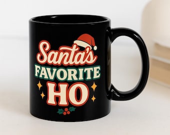 May include: Black ceramic mug with the text "Santa's Favorite HO" in red, green, and cream lettering, with a Santa hat graphic. The mug has a curved handle and is likely for beverages.