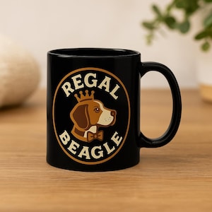 Peut inclure: Mug en céramique noire avec un beagle marron et blanc portant une couronne et un nœud papillon, avec les mots "REGAL BEAGLE" dans un design circulaire. La tasse a une anse incurvée et est posée sur une surface en bois.