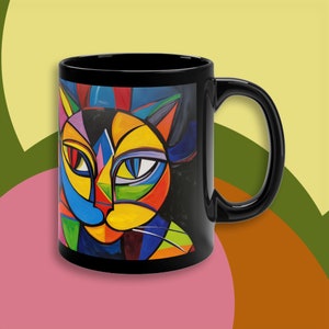 May include: Black coffee mug with a colorful abstract cat design. The cat's face is made up of geometric shapes in shades of blue, green, yellow, red, and orange.