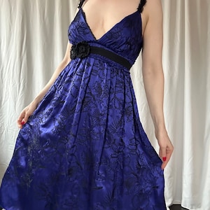 May include: A blue satin dress with black floral embroidery and a black ribbon at the waist.