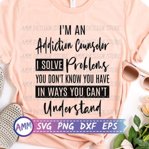 Puede incluir: Una camiseta de color melocotón con texto negro que dice "Soy un consejero de adicciones Resuelvo problemas que no sabes que tienes De maneras que no puedes entender". El texto está rodeado por un borde blanco. La camiseta está colocada sobre una superficie blanca con un par de zapatos beige y gafas de sol.