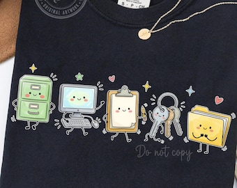 May include: A black t-shirt featuring a graphic print of five anthropomorphic office supplies: a green filing cabinet, a computer, a clipboard, a set of keys, and a yellow folder, all with smiling faces, surrounded by small stars and hearts.