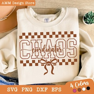 May include: Cream-colored sweatshirt with the words "CHAOS coordinator" in brown block letters, a bow graphic, and a checkered pattern. The image also shows a hat, jeans, and a small plant.