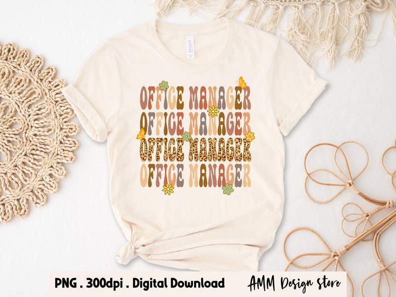 Pode incluir: Uma camiseta bege com o texto "OFFICE MANAGER" repetido quatro vezes em uma fonte retr&ocirc;. Cada palavra est&aacute; em uma cor diferente e tem um design floral ou de borboleta.