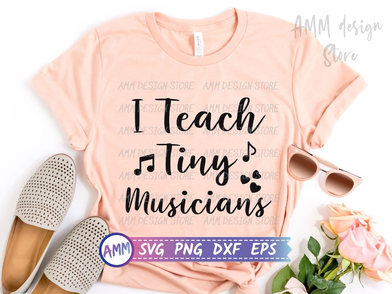 May include: A peach-colored t-shirt with the text "I Teach Tiny Musicians" in black. The text is in a cursive font and includes musical notes and hearts. The shirt is on a white background with a pair of sunglasses, a bouquet of pink roses, and two pairs of shoes.