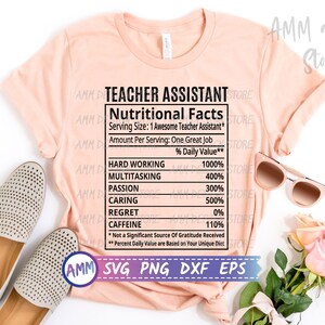 May include: A pink t-shirt with the text "Teacher Assistant Nutritional Facts" and a list of qualities with percentages. The text includes "Hard Working 1000%", "Multitasking 400%", "Passion 300%", "Caring 500%", "Regret 0%", and "Caffeine 110%". The text also includes "*Not a Significant Source of Gratitude Received" and "**Percent Daily Value are Based on Your Unique Diet".