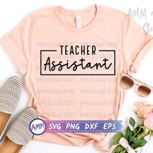 May include: A pink t-shirt with the text "TEACHER-Assistant" in black lettering on a white rectangle. The shirt is laid flat on a white surface with a pair of beige shoes, sunglasses, and pink flowers.