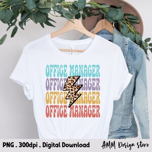 Pode incluir: Uma camiseta branca com o texto "OFFICE MANAGER" repetido quatro vezes em um esquema de cores arco-&iacute;ris. Um gr&aacute;fico de raio com estampa de leopardo est&aacute; centralizado entre o texto.