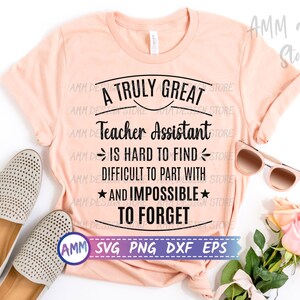 May include: A peach-coloured t-shirt with black text that reads "A Truly Great Teacher Assistant Is Hard To Find, Difficult To Part With, And Impossible To Forget". The text is surrounded by a black circle. The shirt is laid flat on a white surface with a pair of brown shoes and a bouquet of pink roses.