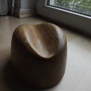 Könnte beinhalten: Ein hölzerner Hutblock mit gewölbter Oberseite und rundem Sockel. Der Hutblock besteht aus hellbraunem Holz und weist eine sichtbare Holzmaserung auf. Er steht auf einem hellen Holzboden.